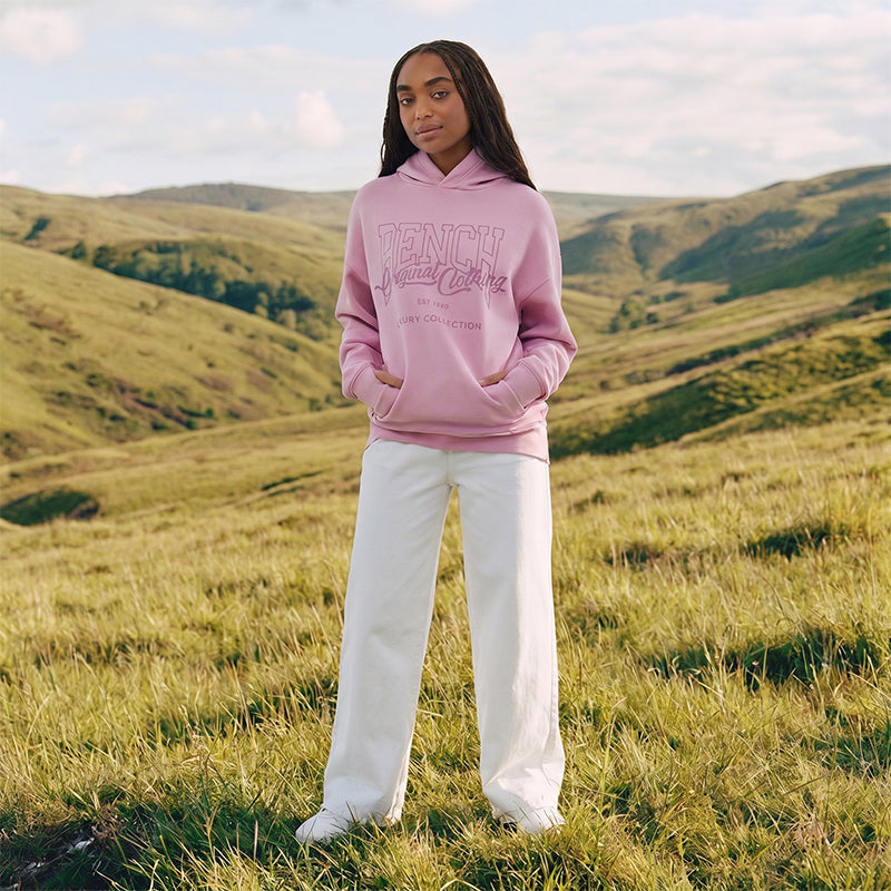 Person wearing a pink hoodie with text standing in a grassy field