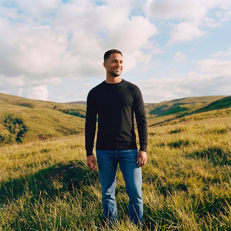 Man standing in a grassy field with a blue sky and clouds