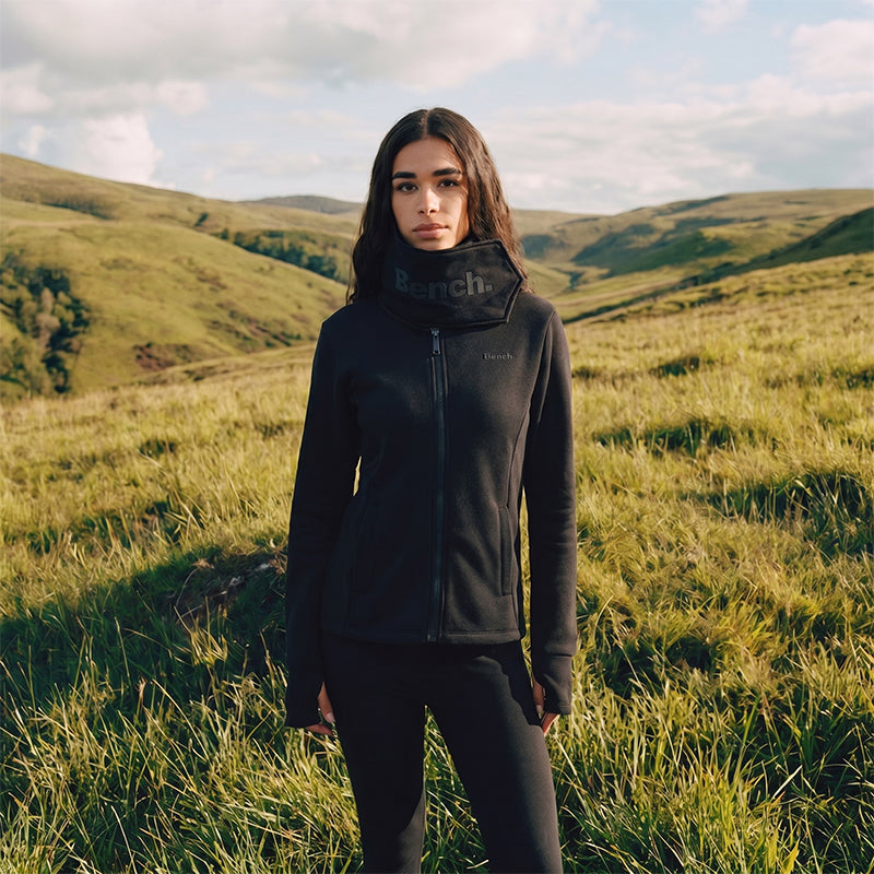 Person wearing a black jacket with a brand logo in a grassy field